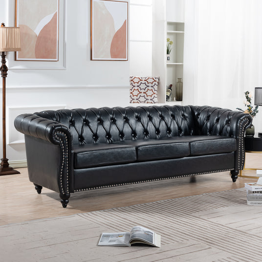 Black faux-leather Chesterfield sofa in a living room, angled view