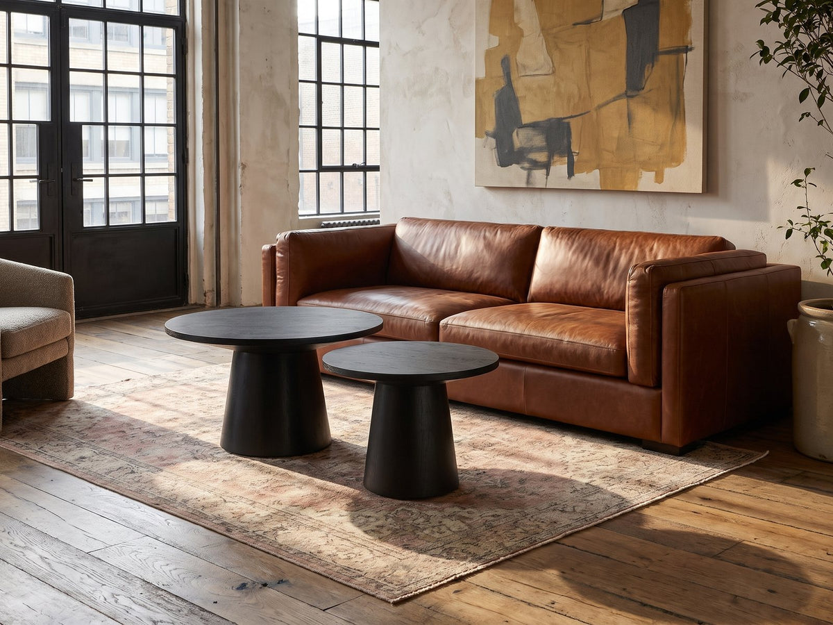 Acqui 29-Inch Round Ebony Oak Veneer Pedestal Coffee and End Table Set on a vintage rug in front of a leather sofa in an industrial loft
