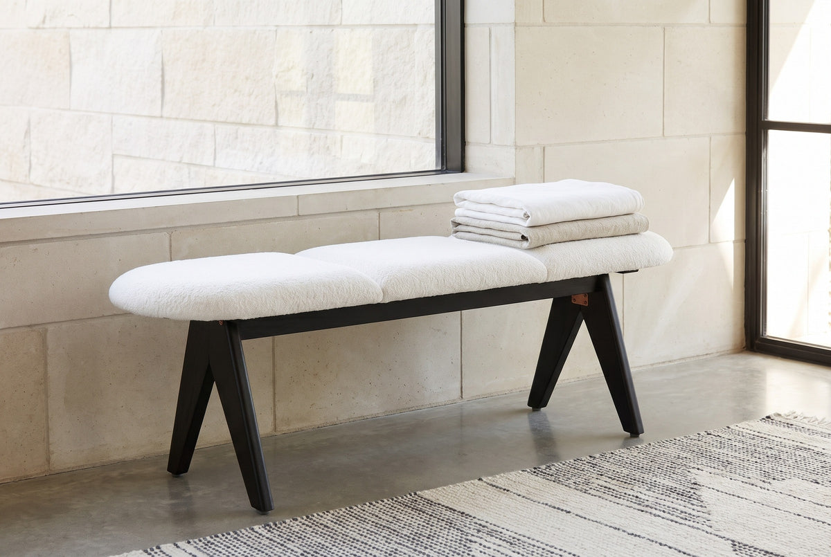 Alatri white fabric bench under a long window ledge on a pale limestone wall in a Dallas living room, with folded blankets on the seat and a wool rug on a concrete floor (blankets and rug not included)