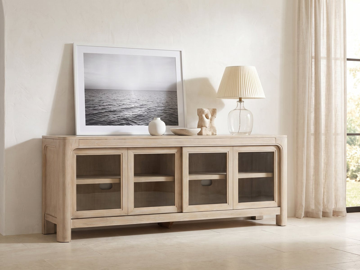 Albenga 71-Inch Weathered Mango Veneer Sliding Glass Door Media Console styled with a leaning print, a lamp and ceramics in a bright plaster room