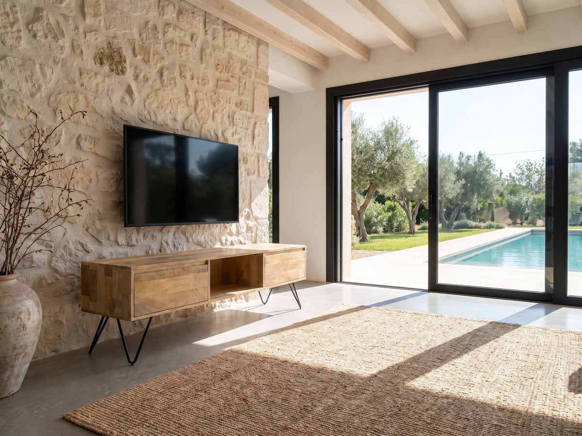 Alberobello Low Mango Media Console seen from the side, under a wall-mounted screen on a pale stone wall in a poolside villa
