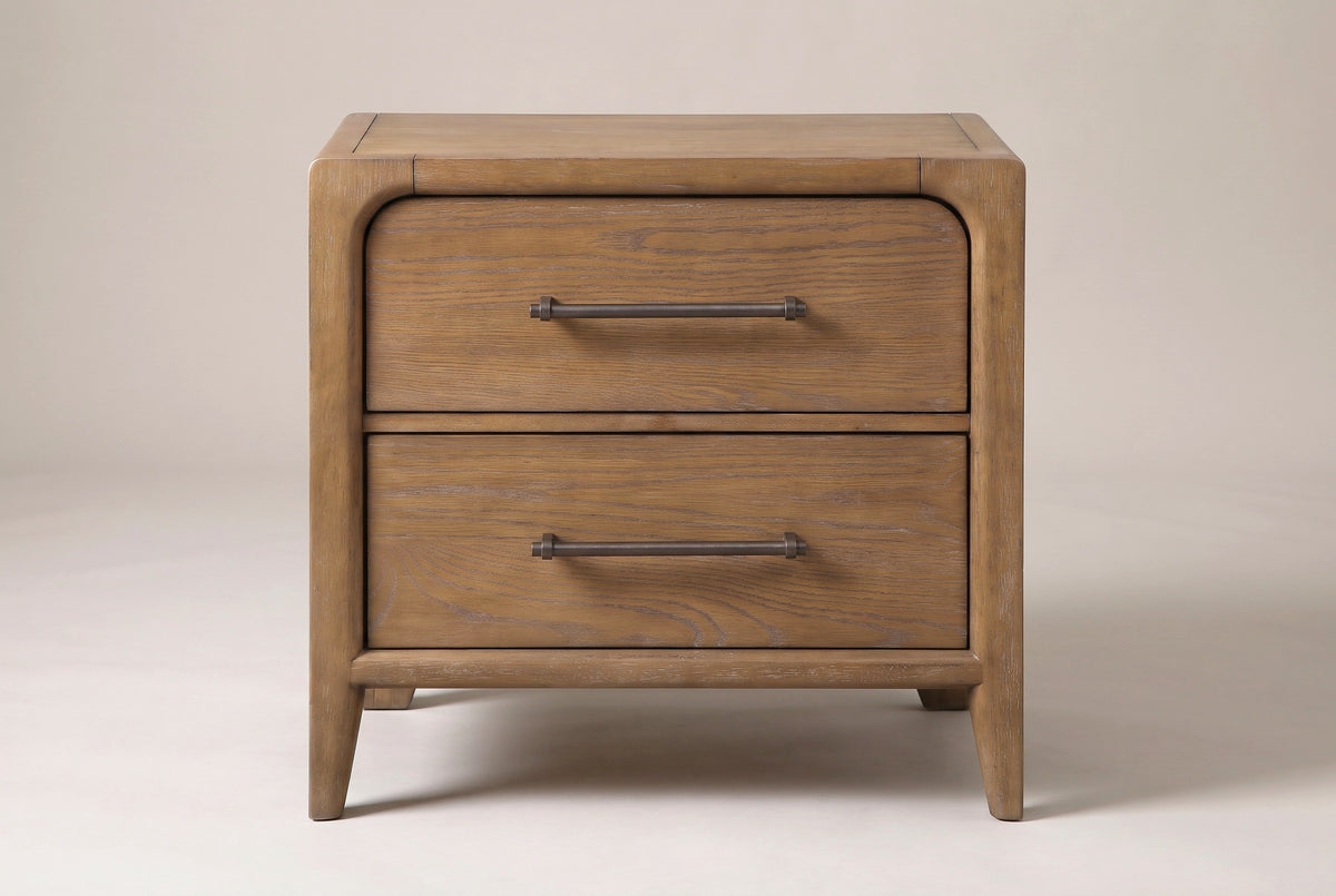 One Alghero nightstand in brown oak, front view on a light studio backdrop: two drawers with bronze bar pulls, a rounded frame and tapered legs