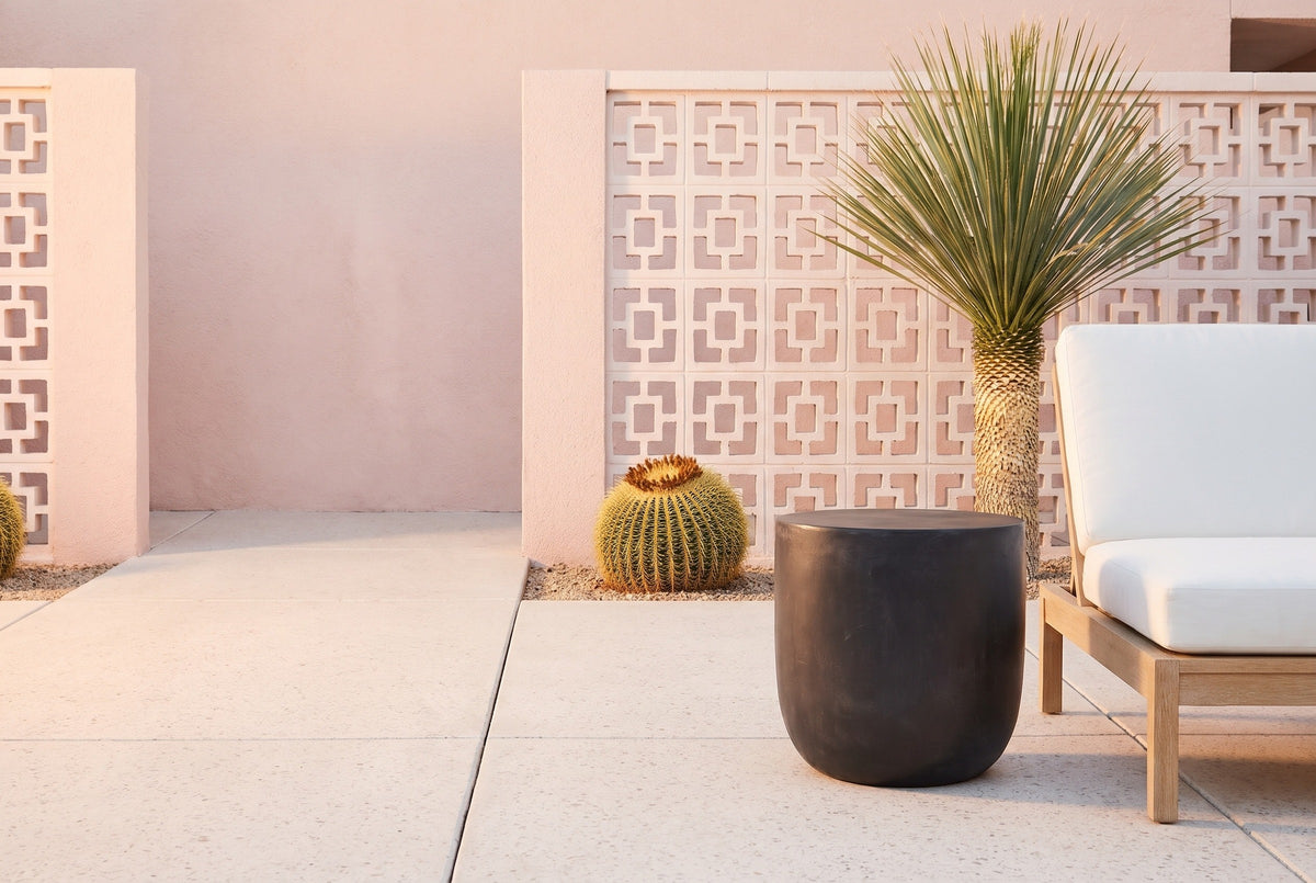 Altavilla matte black concrete side table on a Palm Springs patio, a pink stucco wall, breeze blocks, a barrel cactus and a lounge chair behind (chair not included)