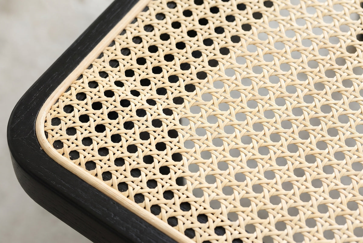 Close-up of the natural rattan cane seat of the Anagni bench: an open weave of small eight-sided openings with a thin cane binding beside the black oak frame
