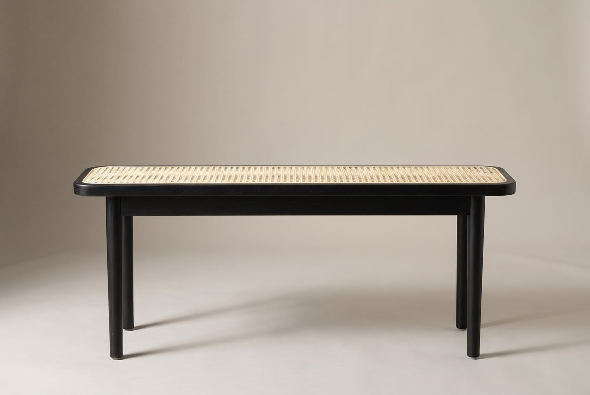 The Anagni bench in black oak with a natural cane seat, side view on a light studio backdrop