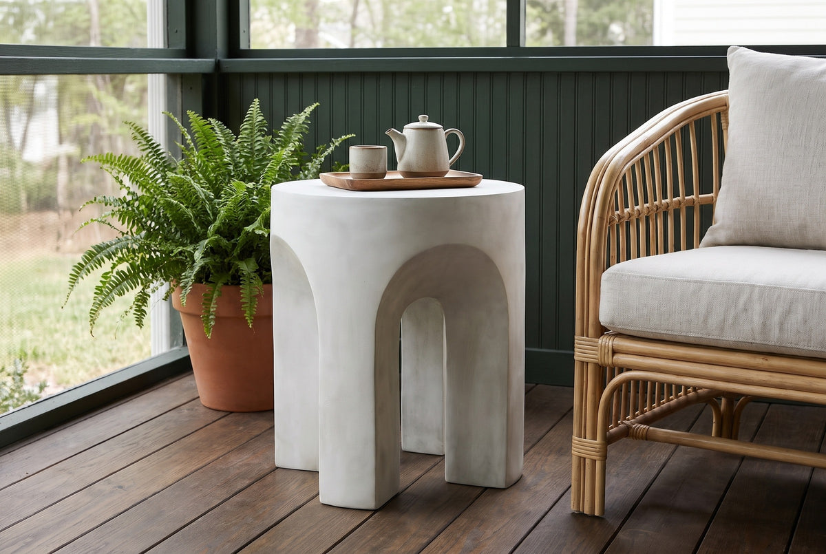 Aragona arched concrete side table with a teapot on a wooden tray on a screened porch in Atlanta, a forest-green beadboard wall and dark oak floor (chair and decor not included)
