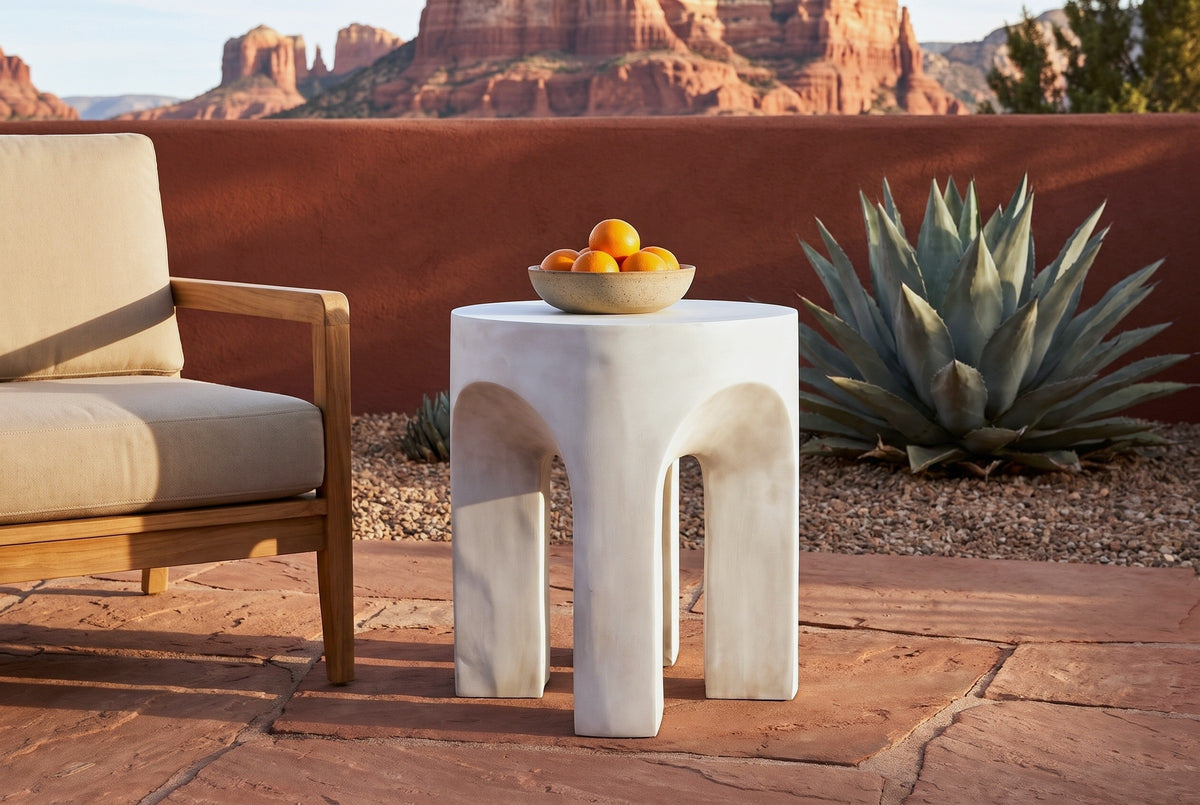 Aragona arched concrete side table with a bowl of oranges on a red sandstone terrace in Sedona at golden hour, a rust-red adobe wall and red rock buttes behind (chair and decor not included)