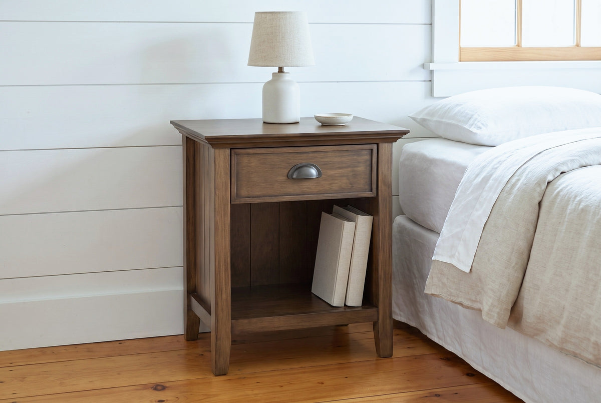 Arbus aged brown nightstand with a ceramic lamp and two linen books in a Vermont farmhouse bedroom with white shiplap walls and pine floors