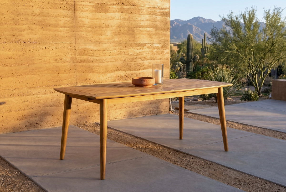 Augusta acacia dining table on concrete pavers on a desert patio at golden hour, a rammed-earth wall, saguaros and mountains behind (chairs not included, bowl and candle holder not included)