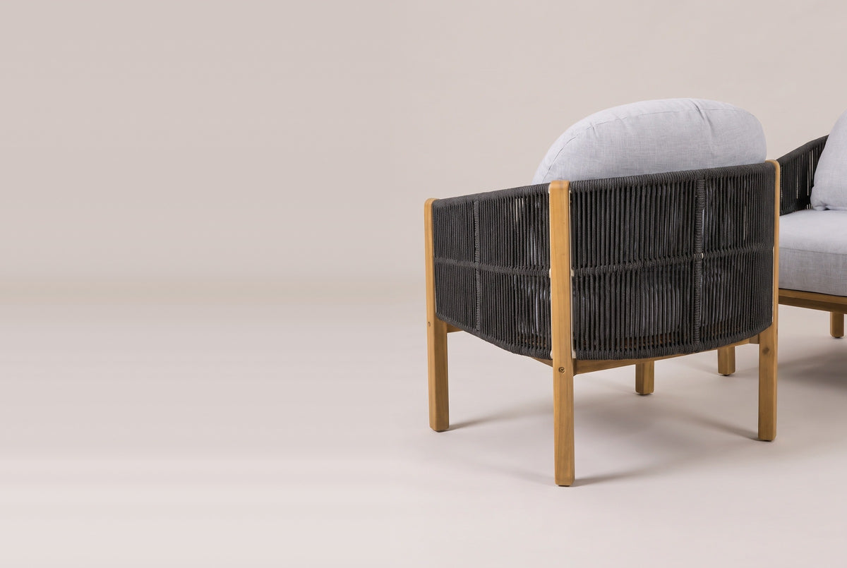 An Avola club chair from behind: the rounded dark gray rope back with its mid-height band, square acacia rear posts and the arched gray back cushion