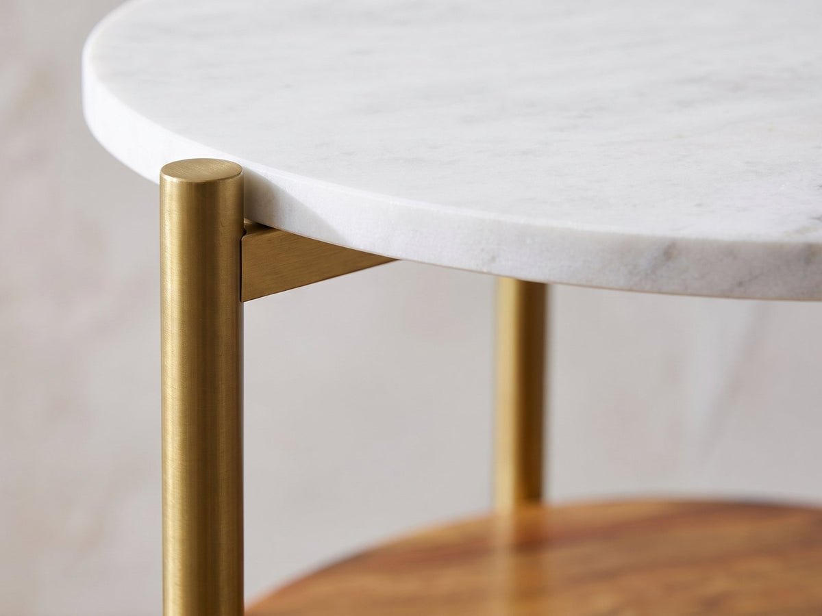 Close-up of the Badolato Marble and Acacia Two-Tier Side Table: the brass-finish leg and bracket under the marble top