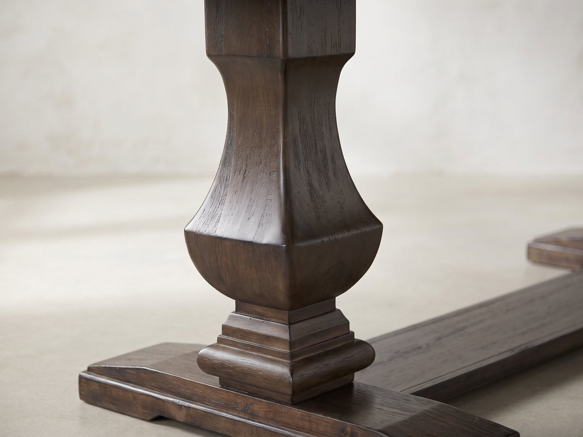 Close-up of the Bagnara 76.5 to 94.5-Inch Rustic Oak Double Pedestal Dining Set with 4 Chairs: the square urn-shaped baluster pedestal and its moulded foot