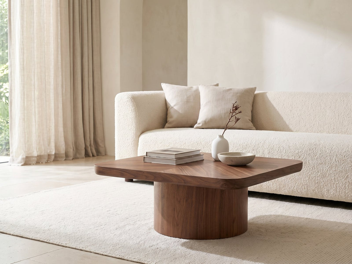 Bari Walnut Veneer Square Pedestal Coffee Table styled with books, a vase and a stone bowl in front of a cream sofa in a bright plaster room
