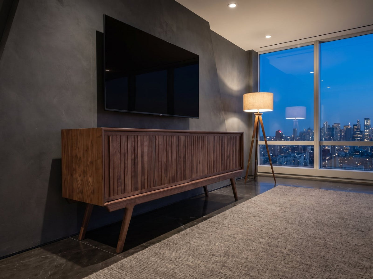 Belluno Solid Walnut Media Cabinet seen from the side, under a wall-mounted screen in a city penthouse at blue hour