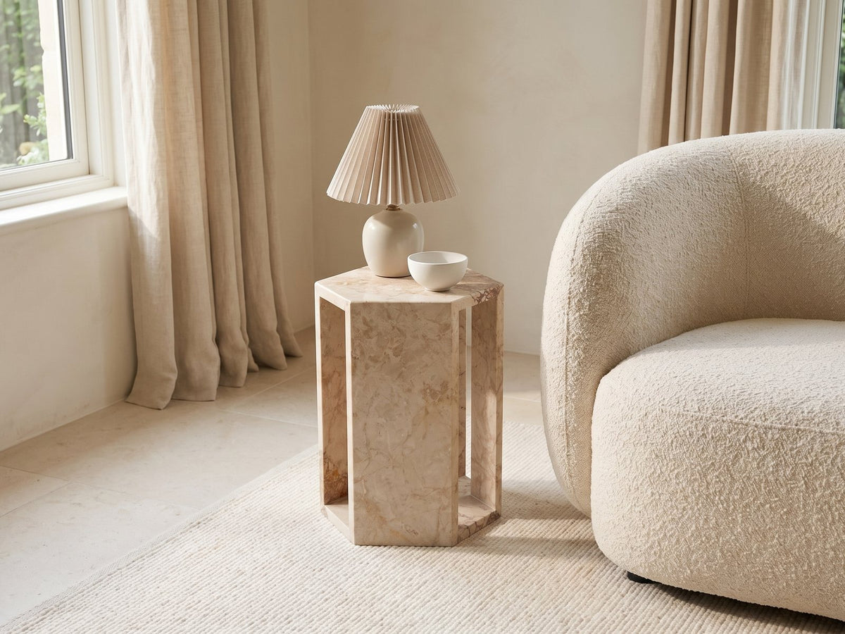 Bojano Rosa Marble Hexagon Side Table with a lamp and a ceramic bowl beside a cream boucle armchair in a bright plaster room