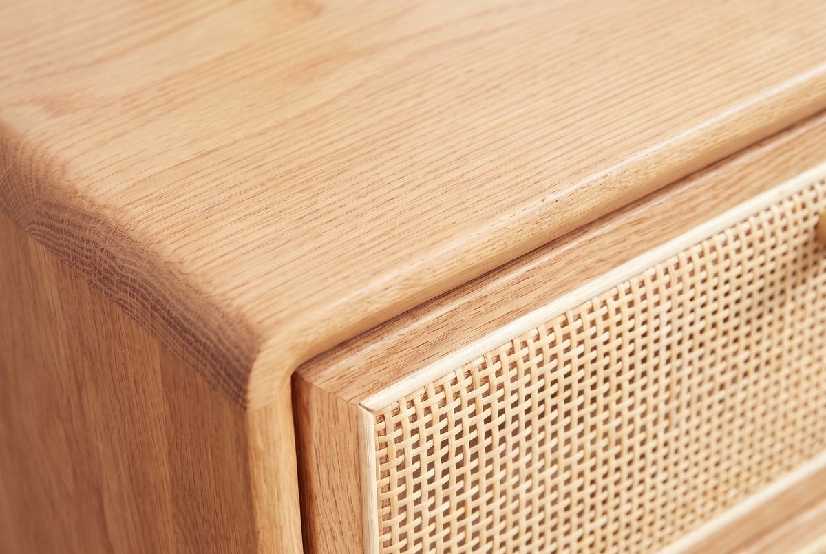 Close-up of the Bono nightstand: light honey oak with fine straight grain, a rounded edge and the woven cane panel