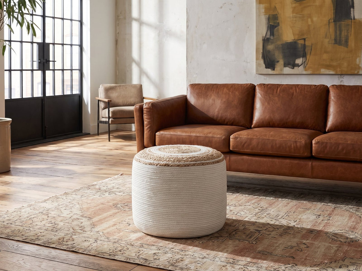 Bordighera Braided Jute and Cotton Round Pouf on a vintage rug in front of a leather sofa in an industrial loft