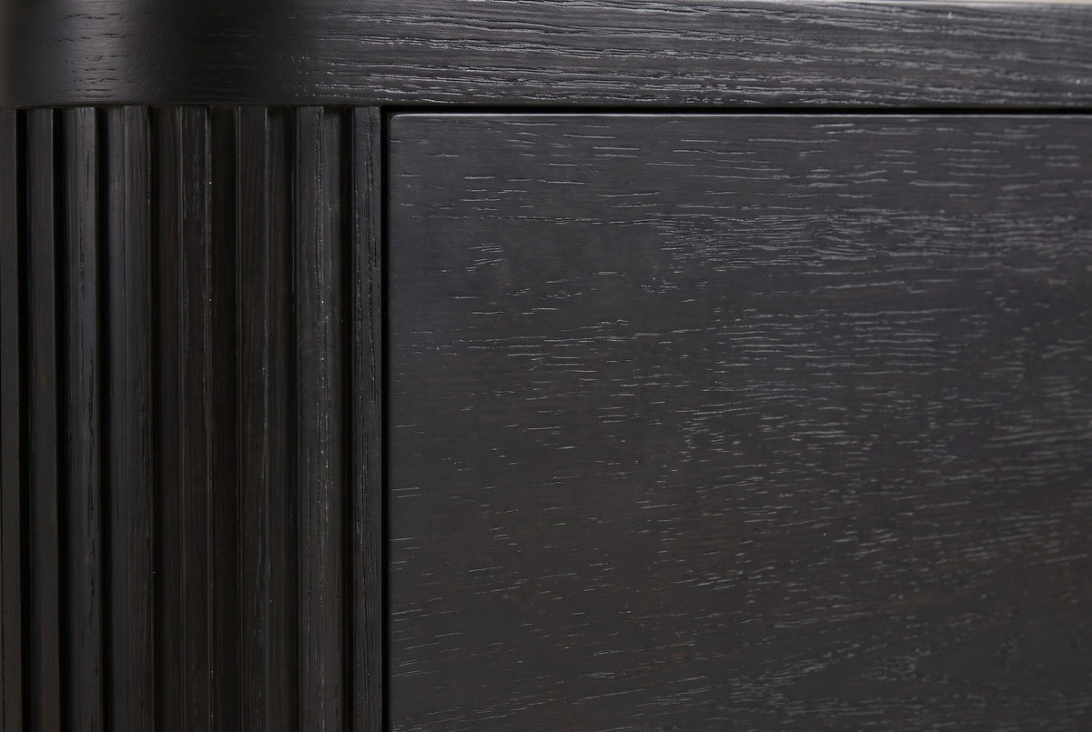 Close-up of the Bosa nightstand: charcoal-stained oak with open grain beside a rounded reeded corner