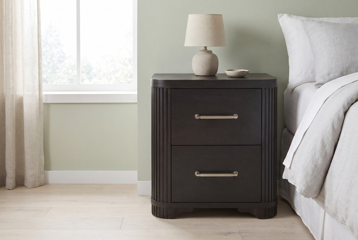 Bosa charcoal oak two-drawer nightstand with a ceramic lamp beside a bed in a Seattle bedroom with a pale sage green wall and a tall linen-curtained window