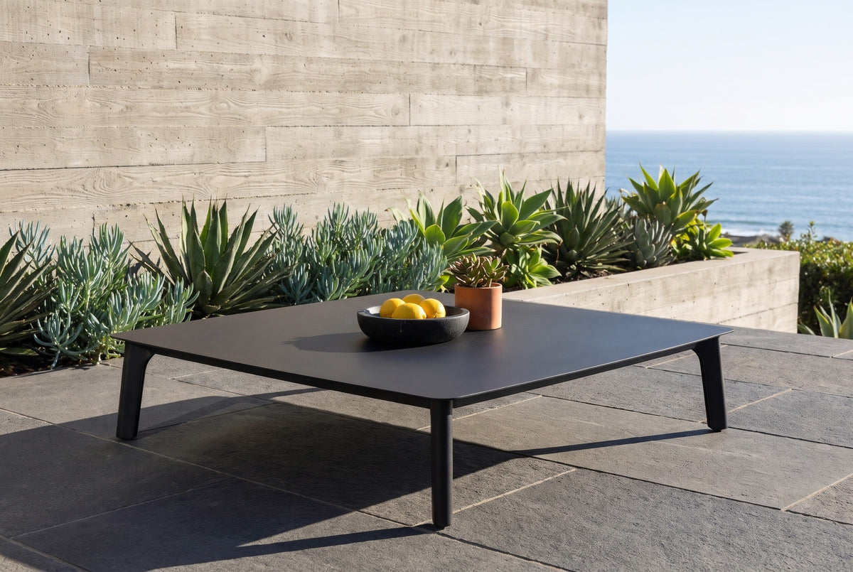 Brucoli black aluminum coffee table on dark basalt pavers at a house in La Jolla, a board-formed concrete wall, agaves and the Pacific behind (bowl and plant not included)