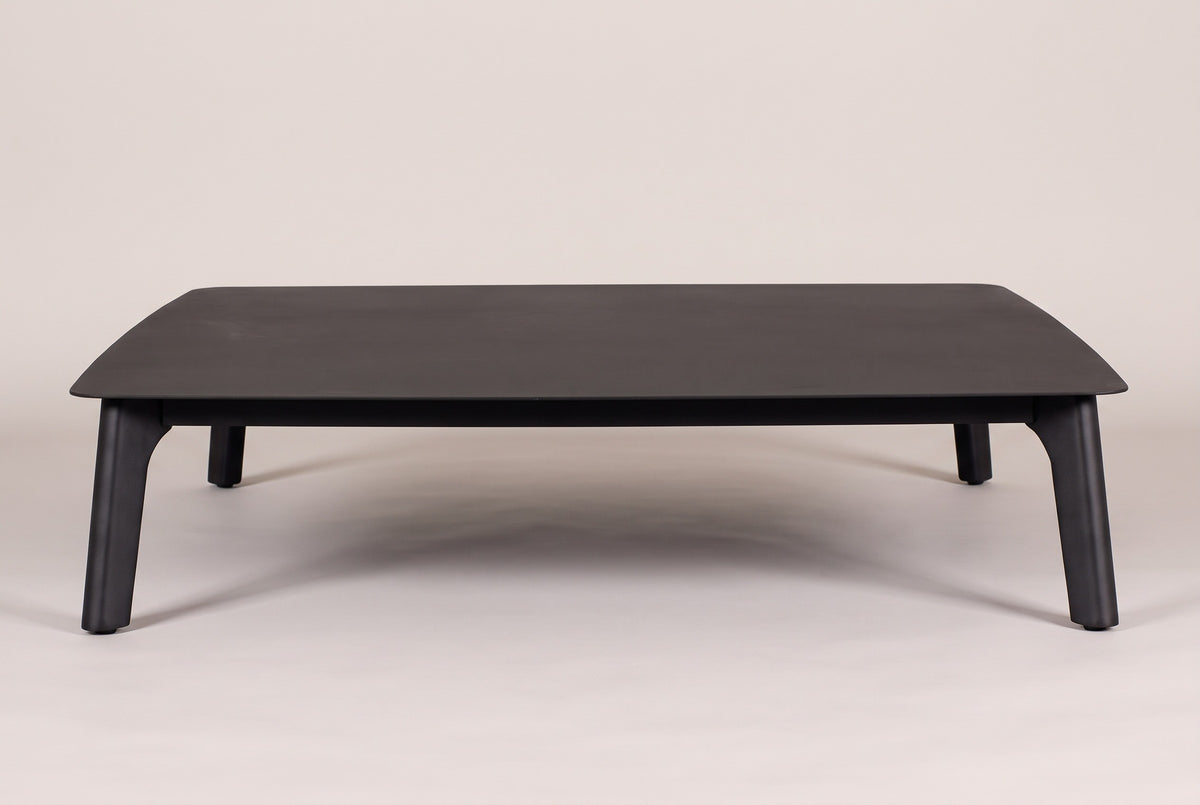The Brucoli coffee table seen from the front: the thin black top with rounded corners on four tapered legs