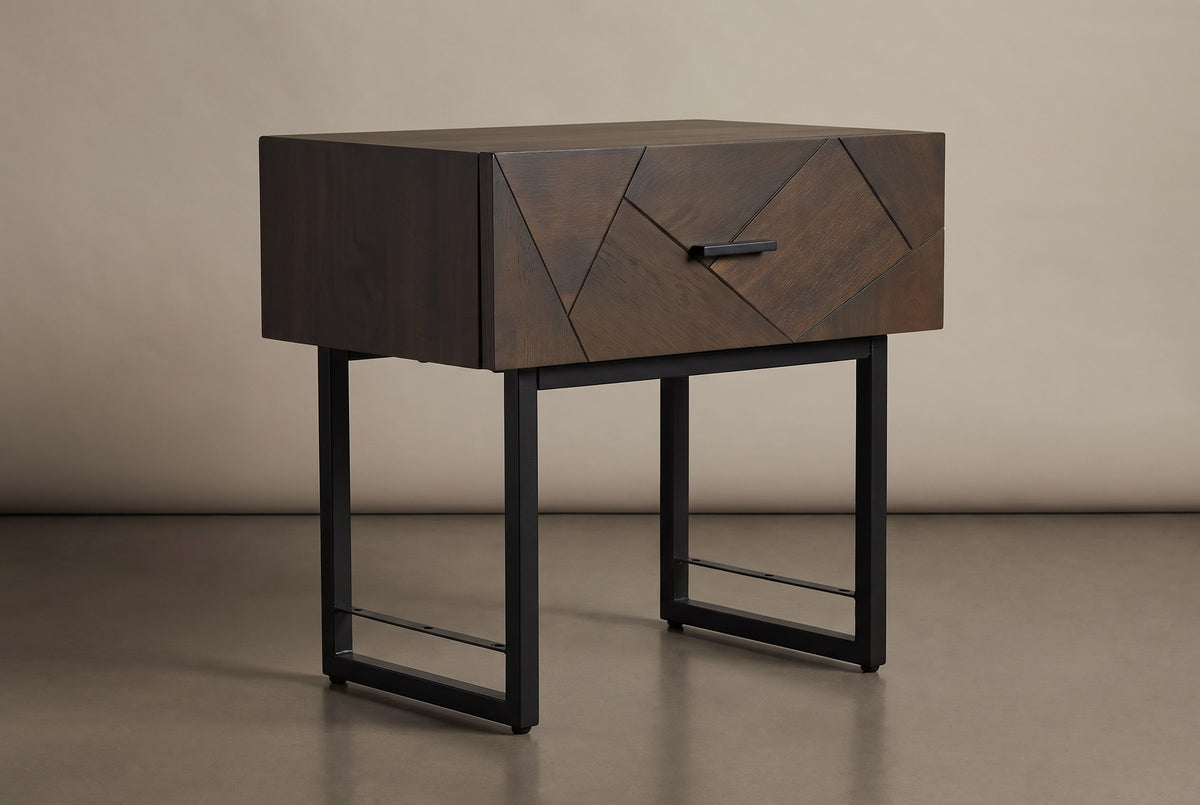 The Budoni one-drawer nightstand in smoked brown oak with an angled inlay front, a black bar pull and a black steel sled base, three-quarter view on a light studio backdrop