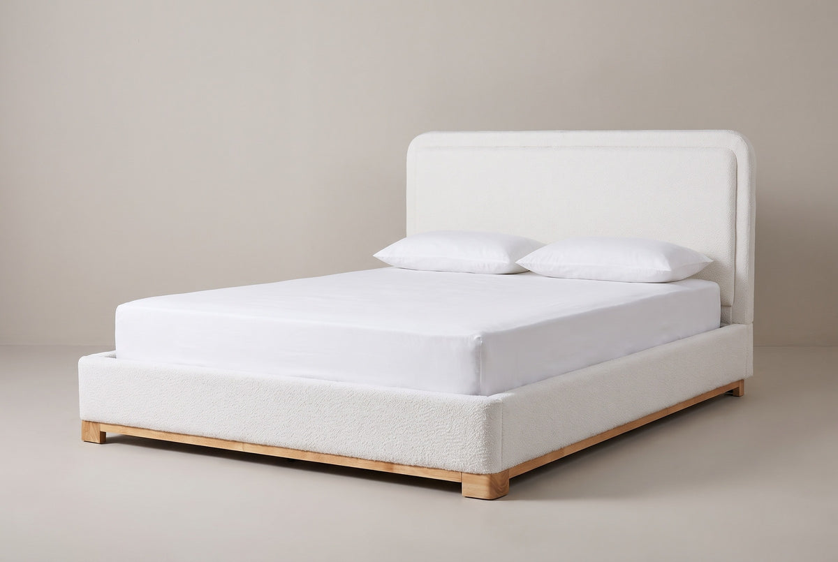 The Bussi bed in white boucle on a light wood plinth with a white mattress and pillows (not included), three-quarter view on a light studio backdrop