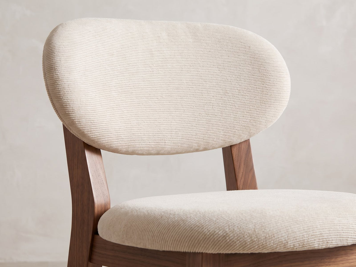 Close-up of the Caccuri 63-Inch Sintered Stone Walnut-Finish Dining Set with 4 Chairs: the oval padded back and round seat of a chair in ivory-beige chenille
