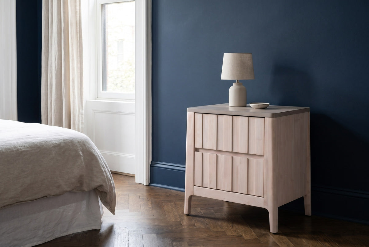 Calangianus whitewash plank two-drawer nightstand with a ceramic lamp beside a bed in a Brooklyn brownstone bedroom with a deep navy plaster wall and a herringbone parquet floor