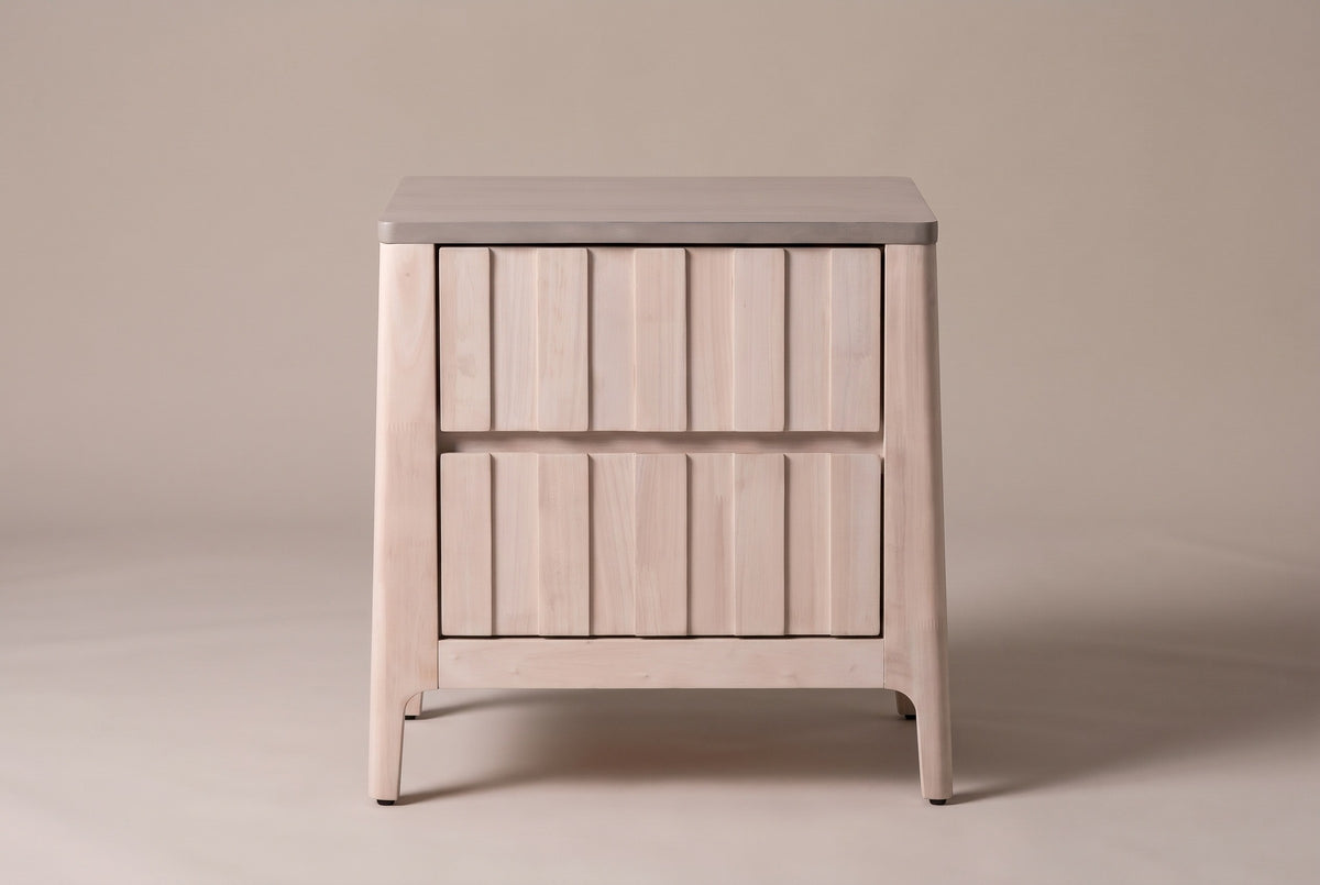 The Calangianus nightstand in pale whitewashed hardwood, front view on a warm greige studio backdrop: two nine-plank drawer fronts, a grey-washed top and four leaning legs