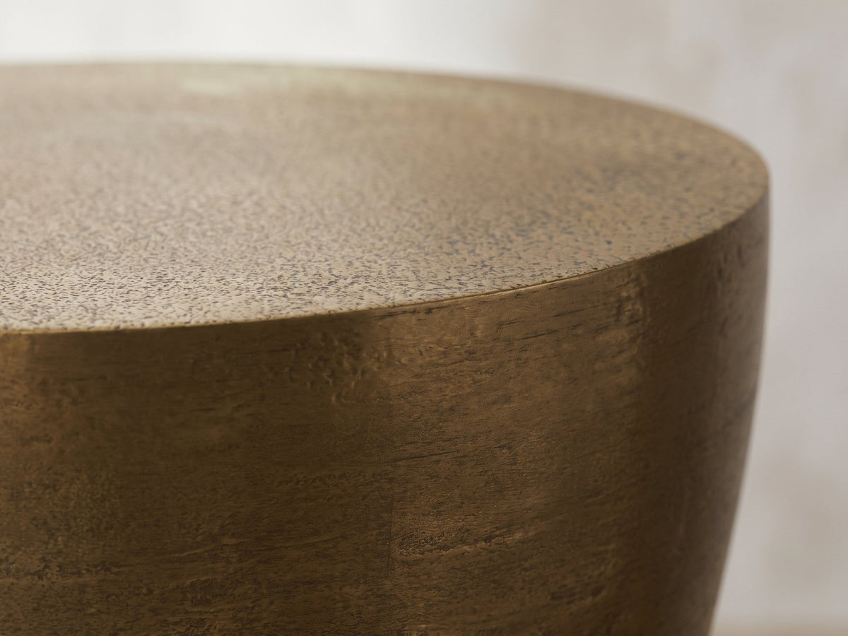 Close-up of the Capestrano Antique Brass Cast Aluminum Drum Side Table: the crisp rim of the top over the curved brass body