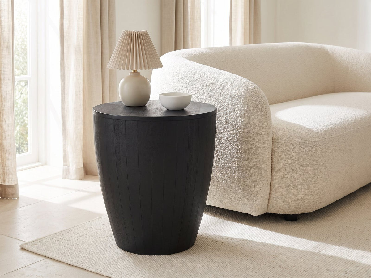 Caramanico Black Mango Tapered Drum Side Table with a lamp and a ceramic bowl beside a cream boucle sofa in a bright plaster room