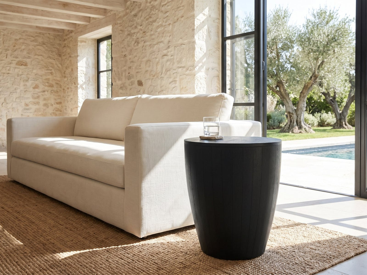 Caramanico Black Mango Tapered Drum Side Table beside a linen sofa in a poolside villa