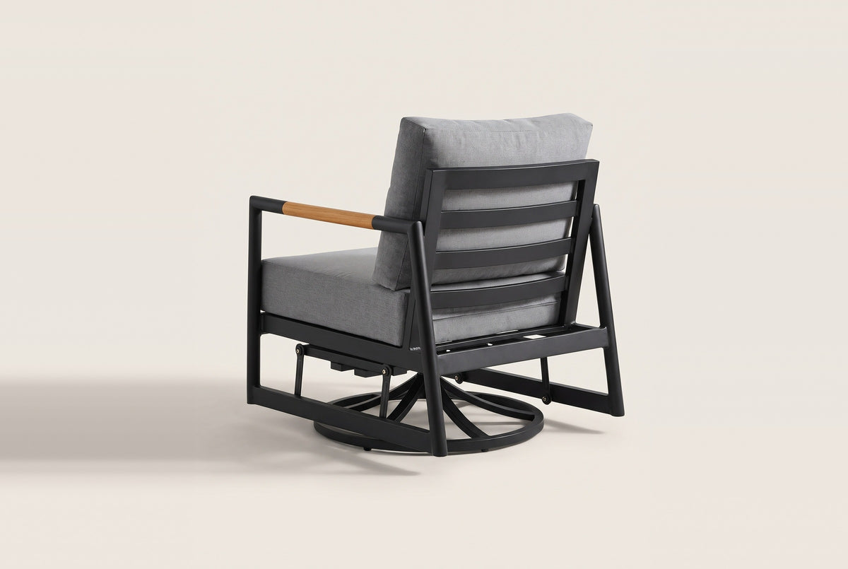 The Carini chair from behind: the black aluminum back frame with three wide slats, the gray back cushion, one teak arm and the swivel glider base