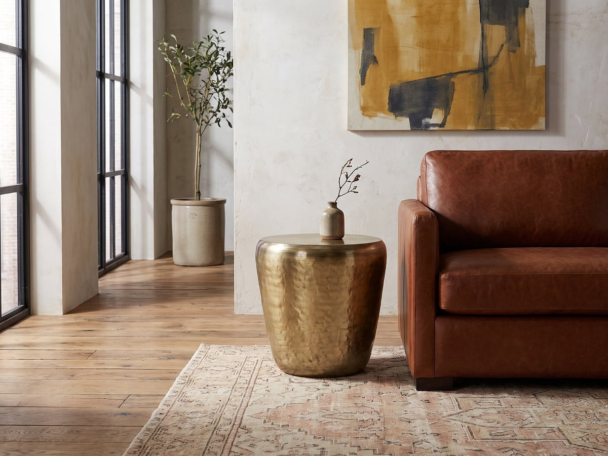 Carovilli Hammered Metal Drum Side Table beside a leather sofa in an industrial loft
