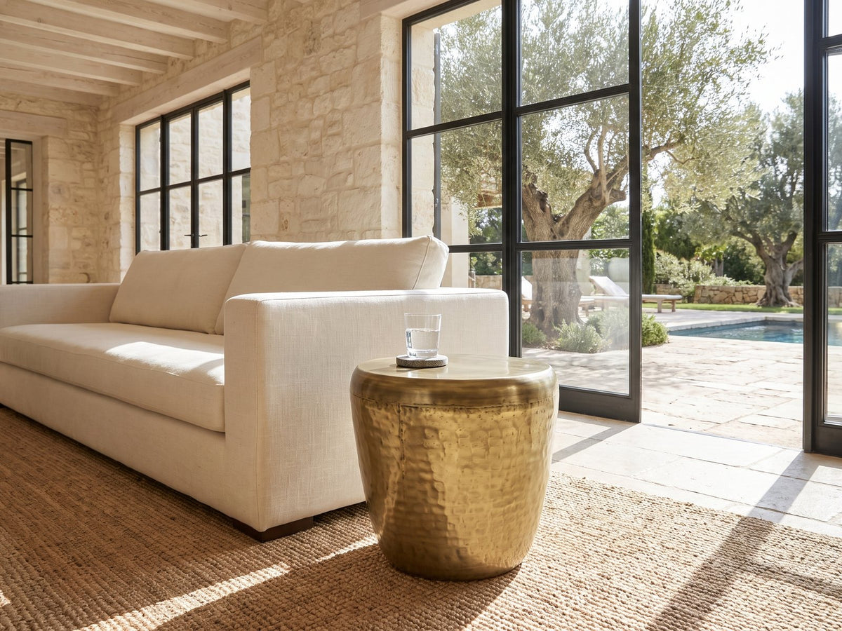 Carovilli Hammered Metal Drum Side Table beside a linen sofa in a poolside villa