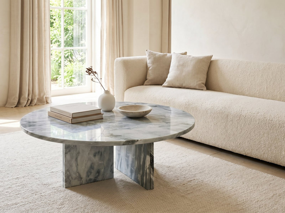 Cascia Compact Blue-Grey Marble Coffee Table styled with books, a vase and a stone bowl in front of a cream sofa in a bright plaster room
