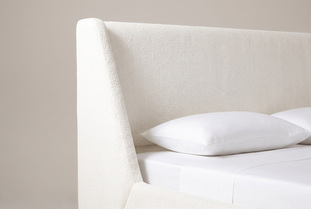 One wing and the plain headboard panel of the Casoli bed in white boucle, above a white pillow