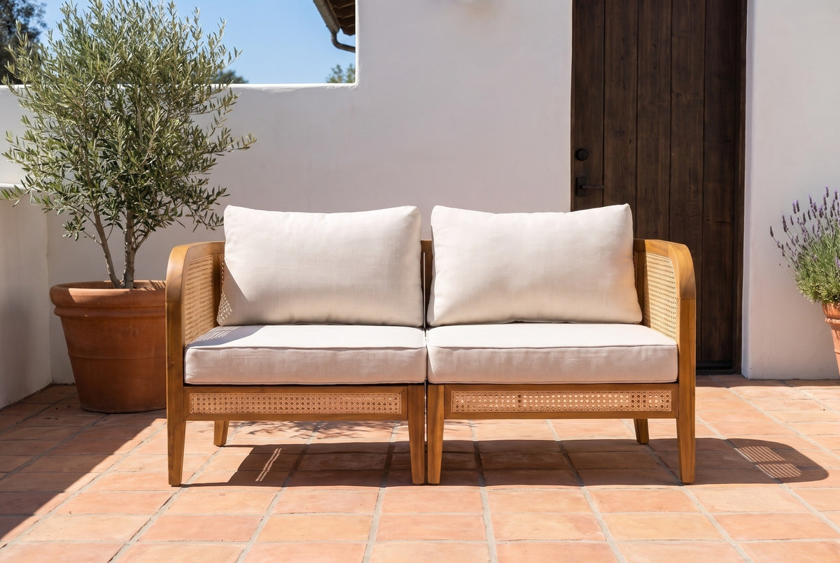 Castelbuono acacia and cane arm chairs joined on a terracotta-tiled terrace at a Santa Barbara house, white stucco wall and a dark wooden door behind (planters not included)