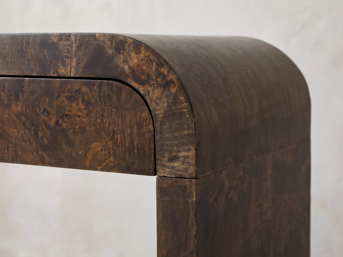 Close-up of the Castellana Burl Veneer Waterfall Console Table: the rounded bend where the burl top curves down to meet a leg, beside the curved corner of a drawer