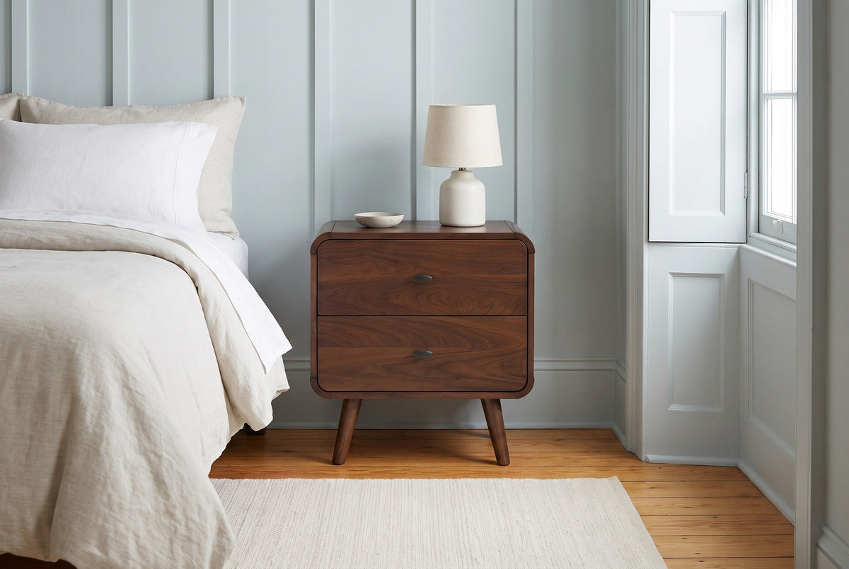 Castelsardo dark walnut nightstand with a ceramic lamp against a haint blue-grey board-and-batten wall in a Charleston bedroom with a heart-pine floor and an ivory rug