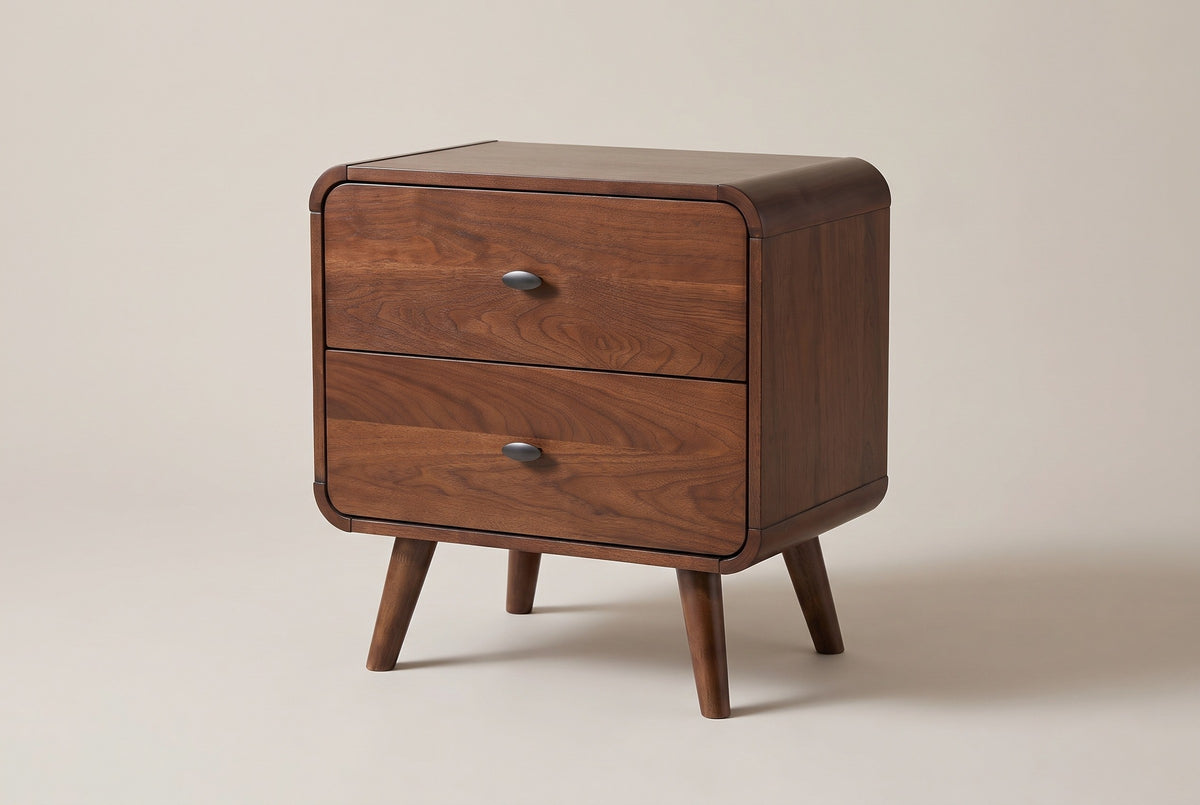 The Castelsardo two-drawer nightstand in dark walnut veneer with rounded rails, oval gunmetal pulls and splayed round legs, three-quarter view on a light greige studio backdrop