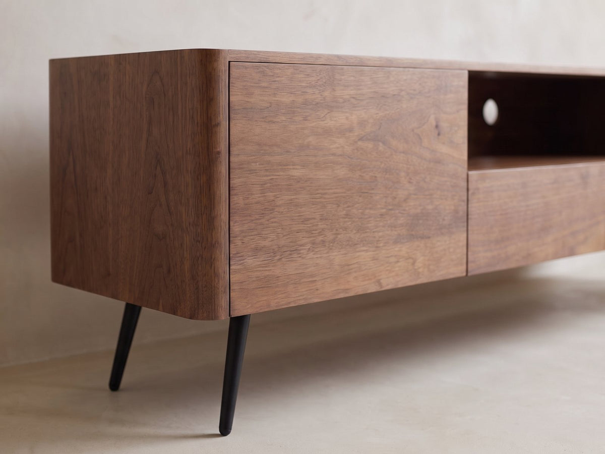 Close-up of the Cernobbio Curved Walnut Media Console: the rounded walnut corner and a slim black tapered leg