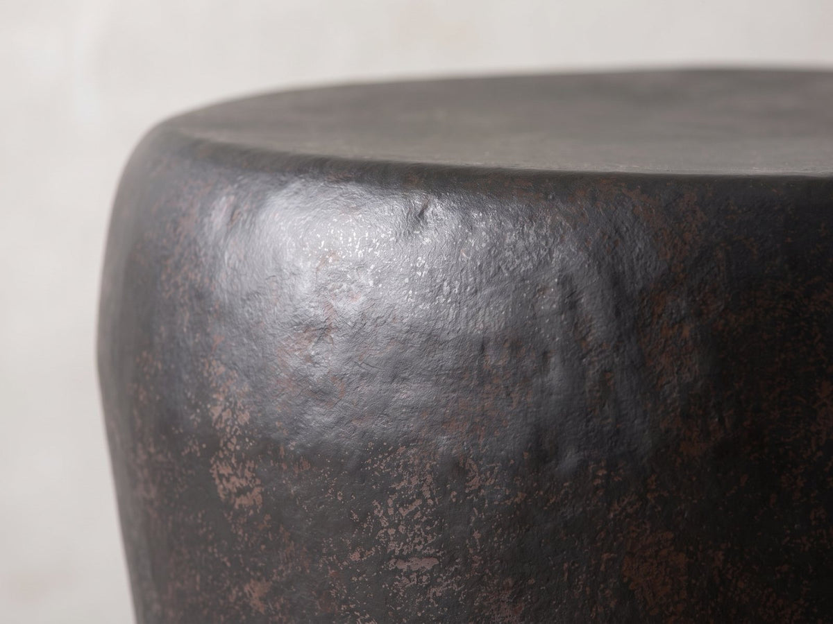 Close-up of the Cervara Rustic Bronze Metal Drum Side Table: the rolled rim and hammered shoulder of the bronze drum