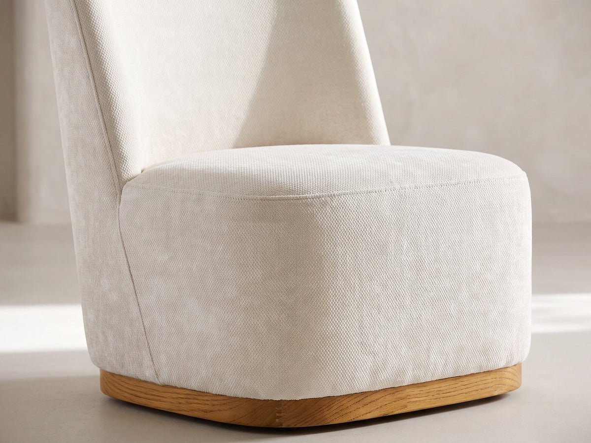 Close-up of the Cetraro 68.75-Inch Fluted Leg Dining Set with 4 Upholstered Chairs: the tall upholstered back and deep seat of a chair in ivory woven fabric on its oak plinth