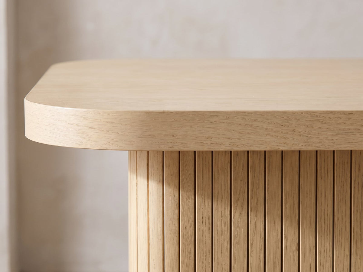 Close-up of the Cetraro 68.75-Inch Fluted Leg Dining Set with 4 Upholstered Chairs: the rounded corner of the oak top over a fluted slab leg