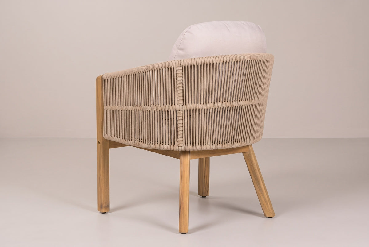 A Chiaramonte dining armchair from behind: the rounded sand-beige rope back with its mid-height band, the back cushion above and the acacia legs