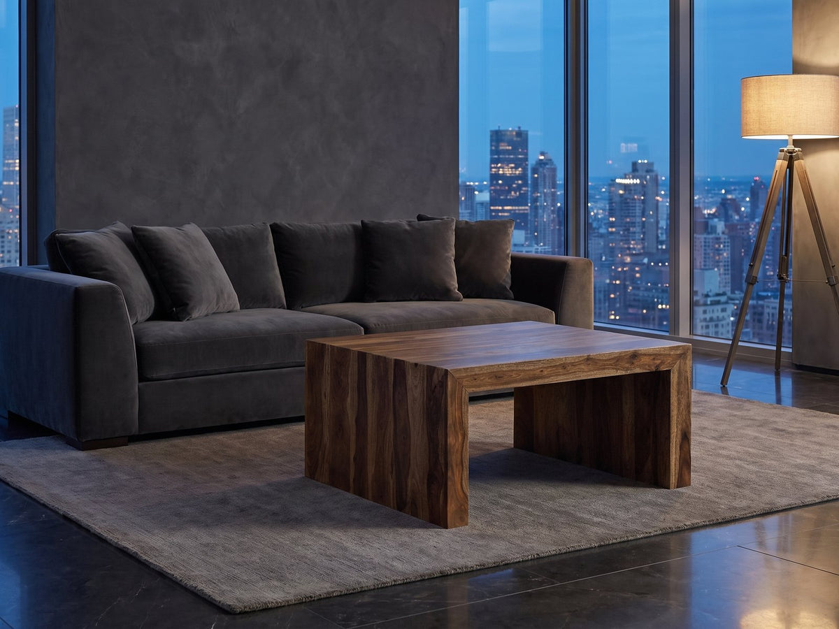 Chieri 34-Inch Square Solid Sheesham Waterfall Coffee Table on a wool rug in front of a velvet sofa in a city penthouse at blue hour