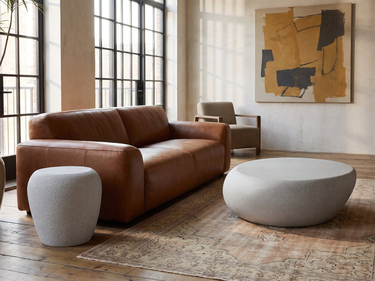 Cilento Grey Fiberglass Pebble Coffee Table and Side Table Set on a vintage rug in front of a leather sofa in an industrial loft