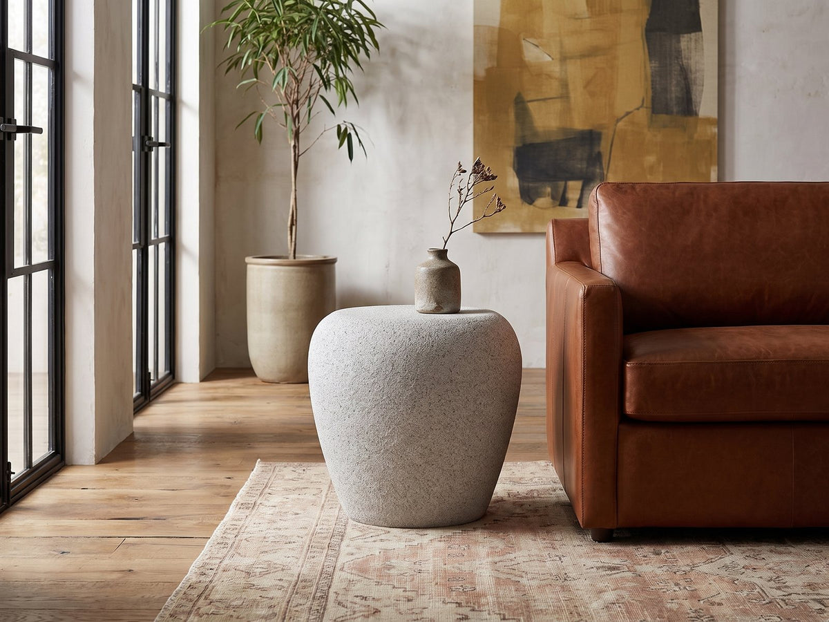 Cilento Speckled Grey Fiberglass Pebble Side Table beside a leather sofa in an industrial loft